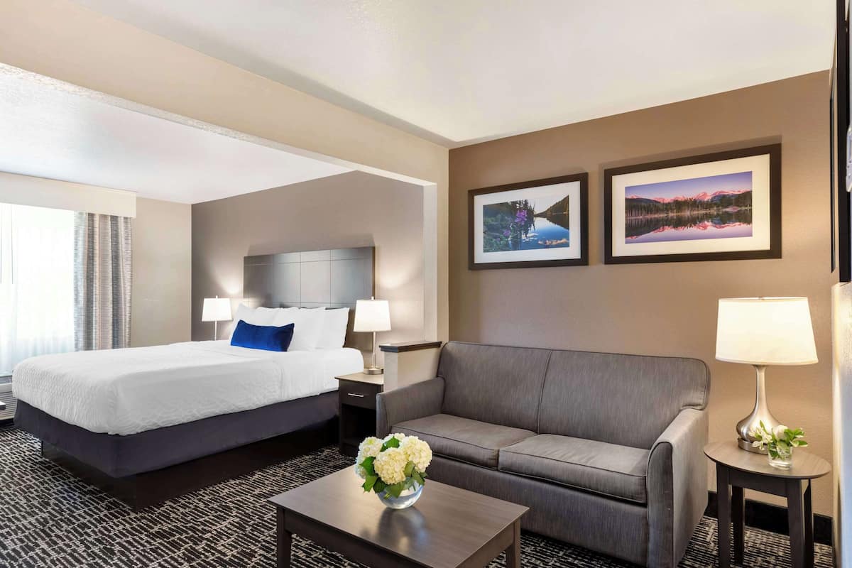 A hotel room with a bed, a sofa, a coffee table, and two framed pictures on the wall.
