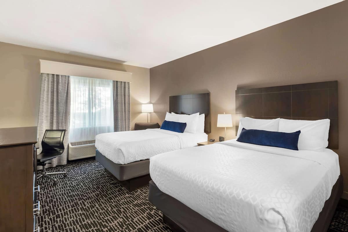 A hotel room with two beds, a desk, and a chair.