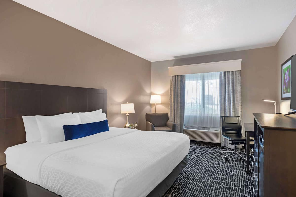 A hotel room with a large bed, two bedside lamps, a desk with a chair, and a window with curtains.