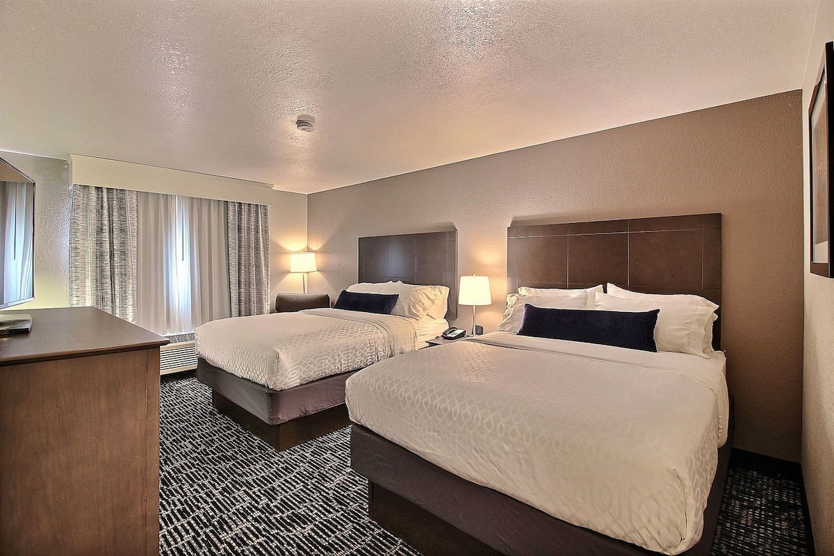 A hotel room with two beds, a desk, and a window with curtains.