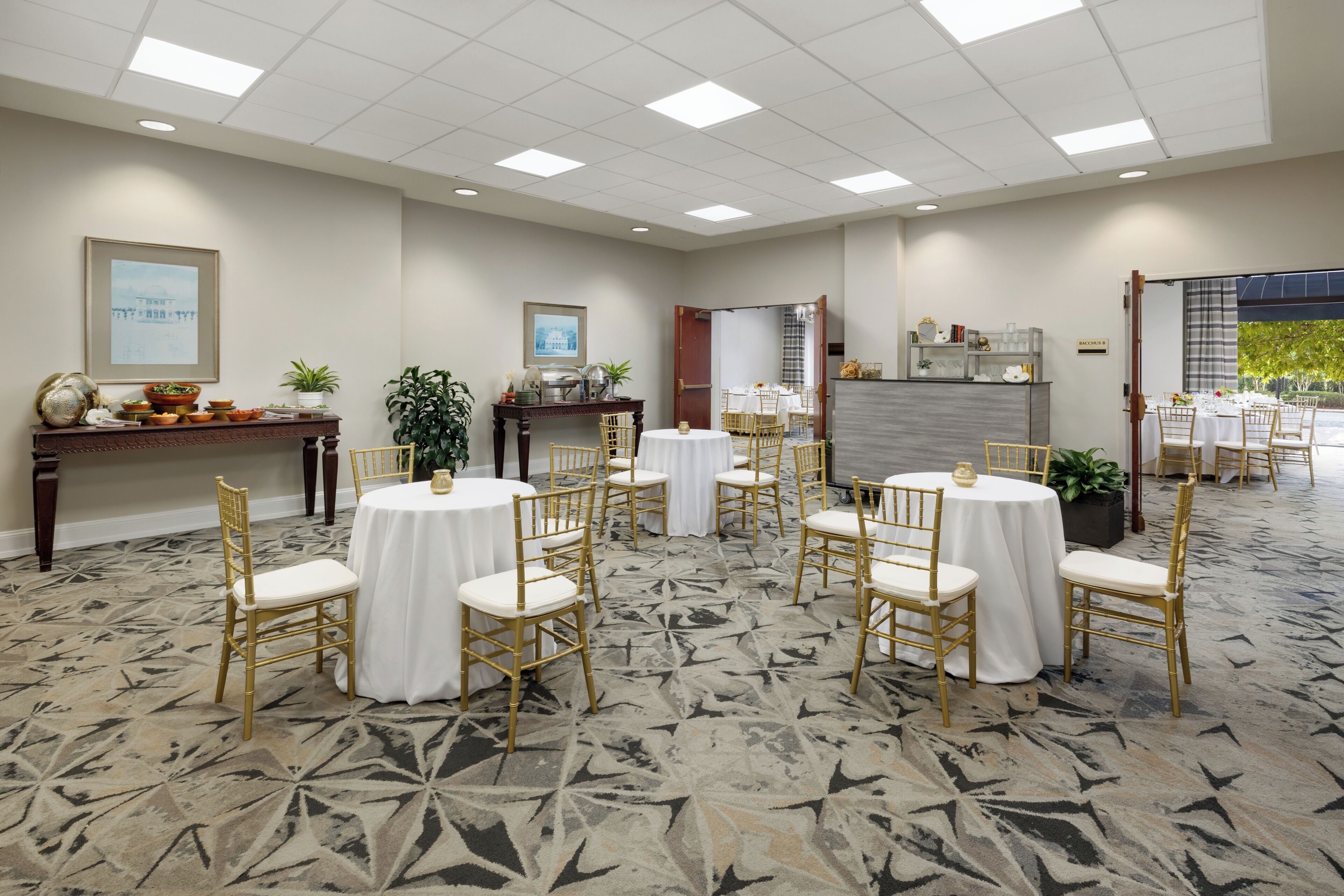 A hotel conference room with round tables, gold chairs, and a patterned carpet.