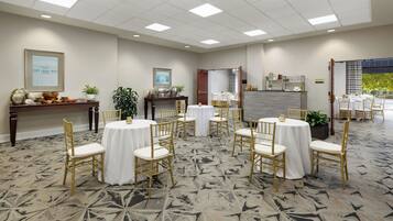 A hotel conference room with round tables, gold chairs, and a patterned carpet.