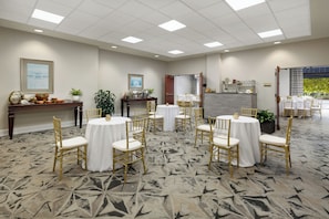 Une salle de conférence d’hôtel avec des tables rondes, des chaises dorées et un tapis à motifs.