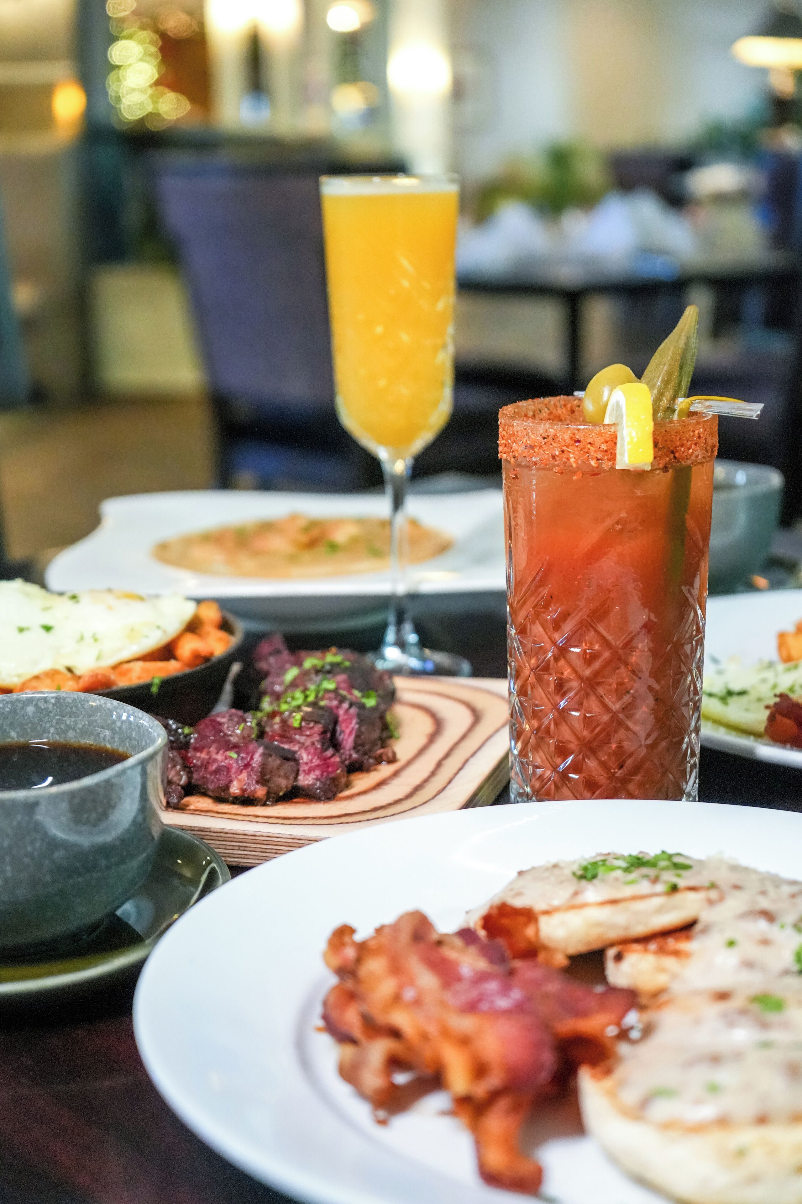 A table with various dishes including a Bloody Mary, a glass of orange juice, and plates of food.