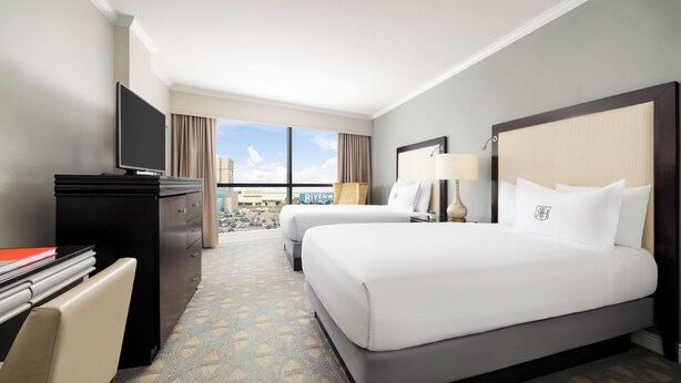 A hotel room with two beds, a desk, a TV, and a view of the city. - The Riverfront Hotel New Orleans (New Orleans)
