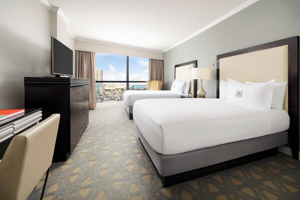 Habitación de hotel con dos camas, un escritorio, un televisor y vistas a la ciudad.