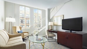 A modern living room with a sofa, a glass coffee table, a television, and a staircase with a railing. - The Riverfront Hotel New Orleans (New Orleans)
