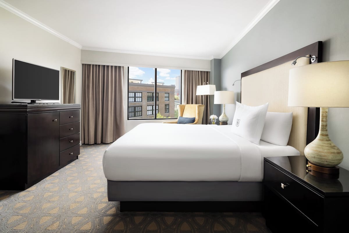 Quarto de hotel com uma cama grande, televisão de tela plana, cômoda e vista da cidade pela janela.