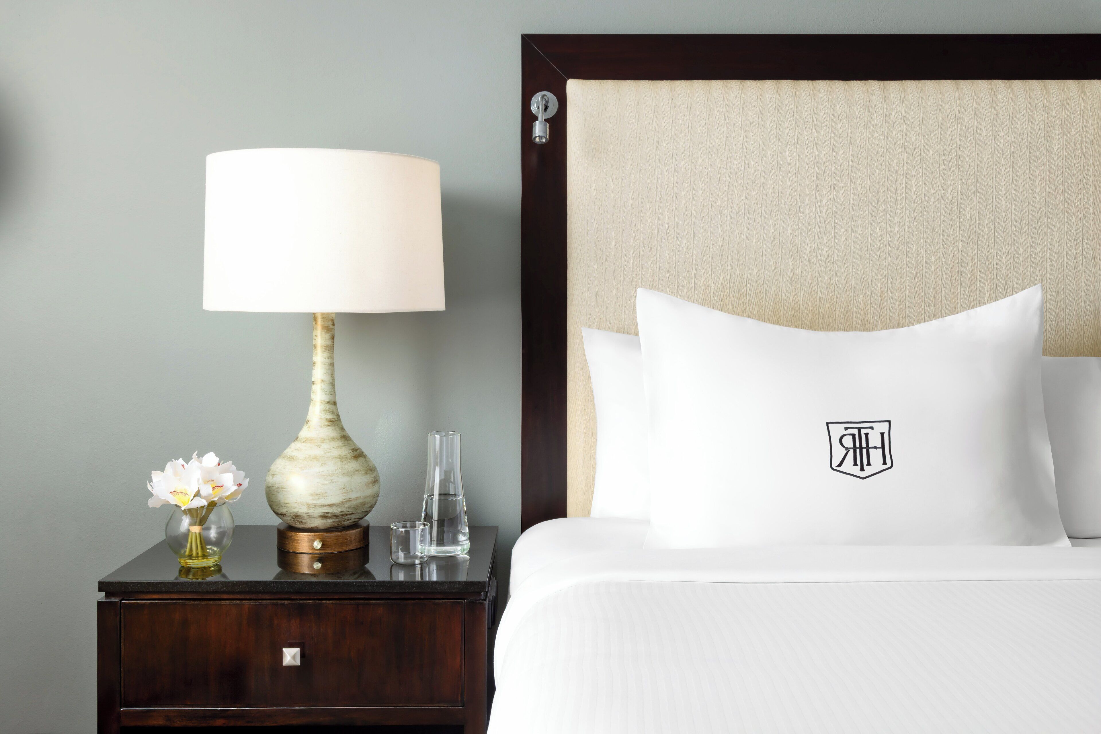 A neatly made hotel room with a bed, a nightstand, a lamp, and a vase with flowers.
