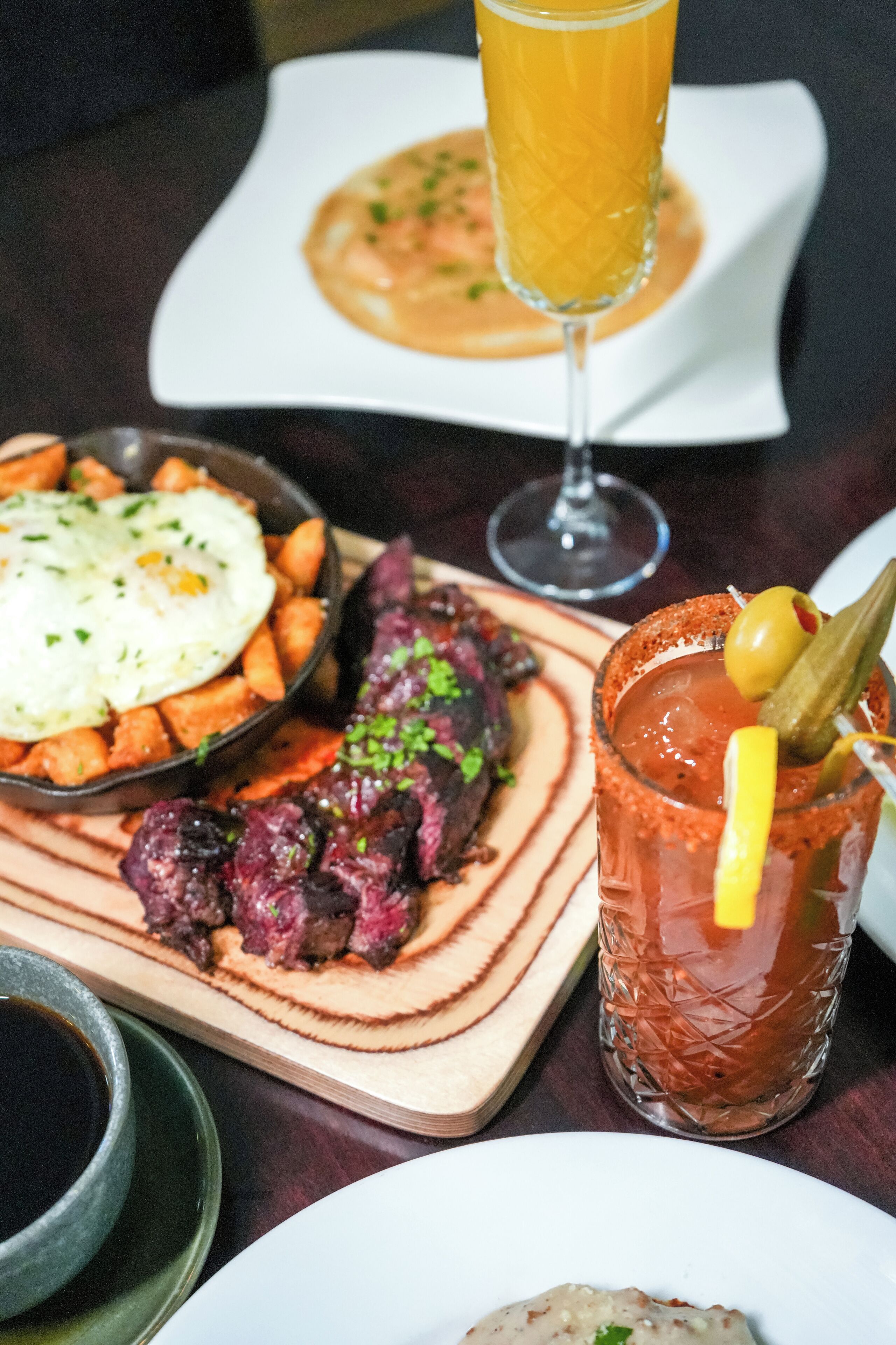 Una mesa con varios platos, incluyendo un vaso de jugo de naranja, un tazón de sopa, un plato de carne y un vaso de bebida roja con una guarnición.