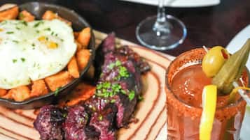 Una mesa con varios platos, incluyendo un vaso de jugo de naranja, un tazón de sopa, un plato de carne y un vaso de bebida roja con una guarnición.