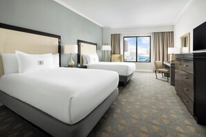 Habitación de hotel con dos camas, televisión, escritorio y vistas a la ciudad.