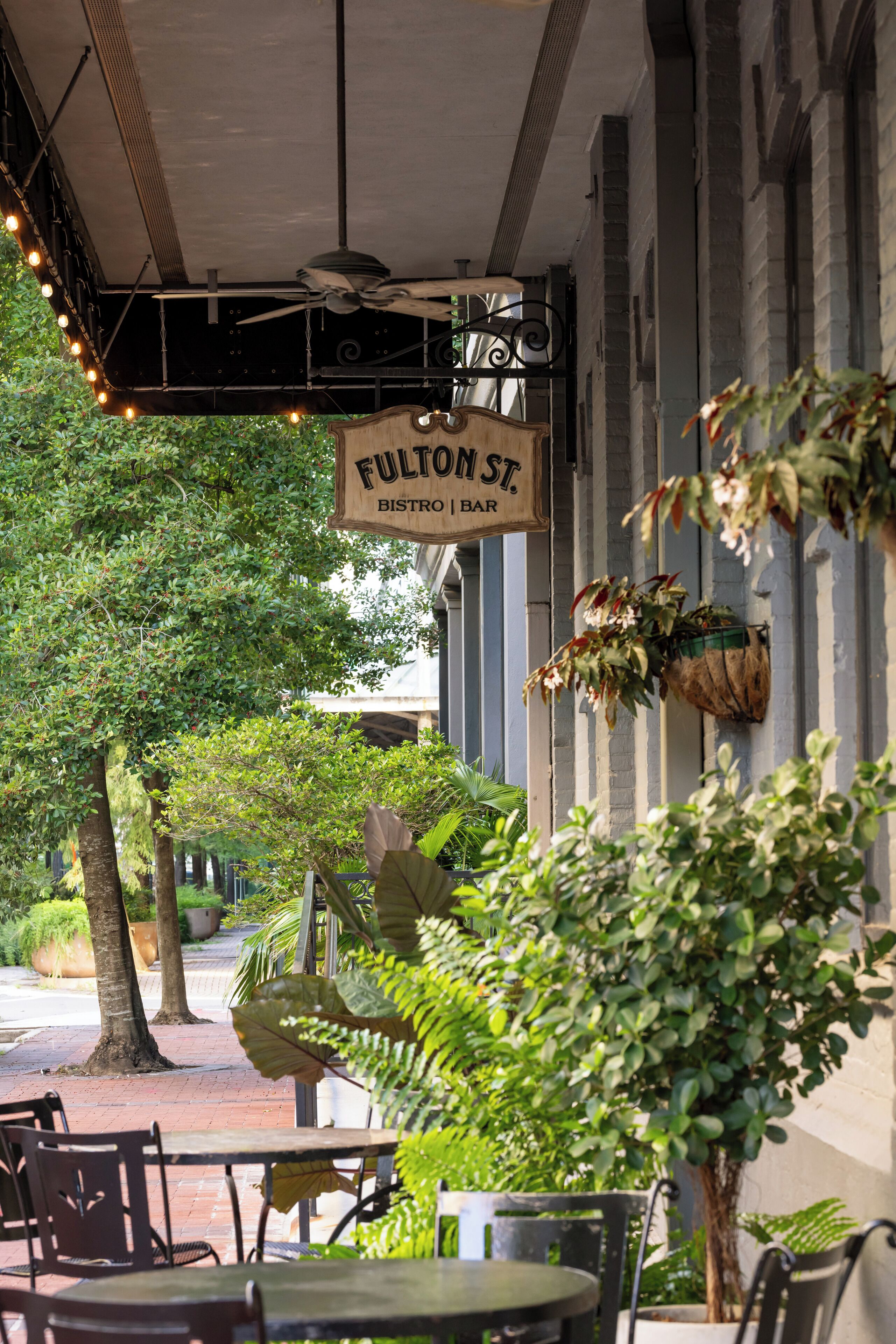 An outdoor seating area with tables and chairs, a hanging sign for Fulton St. Bistro Bar, and a ceiling fan.