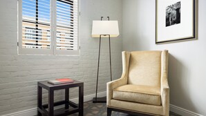 A room with a beige armchair, a small wooden table with a book, a floor lamp, and a window with blinds. - The Riverfront Hotel New Orleans (New Orleans)