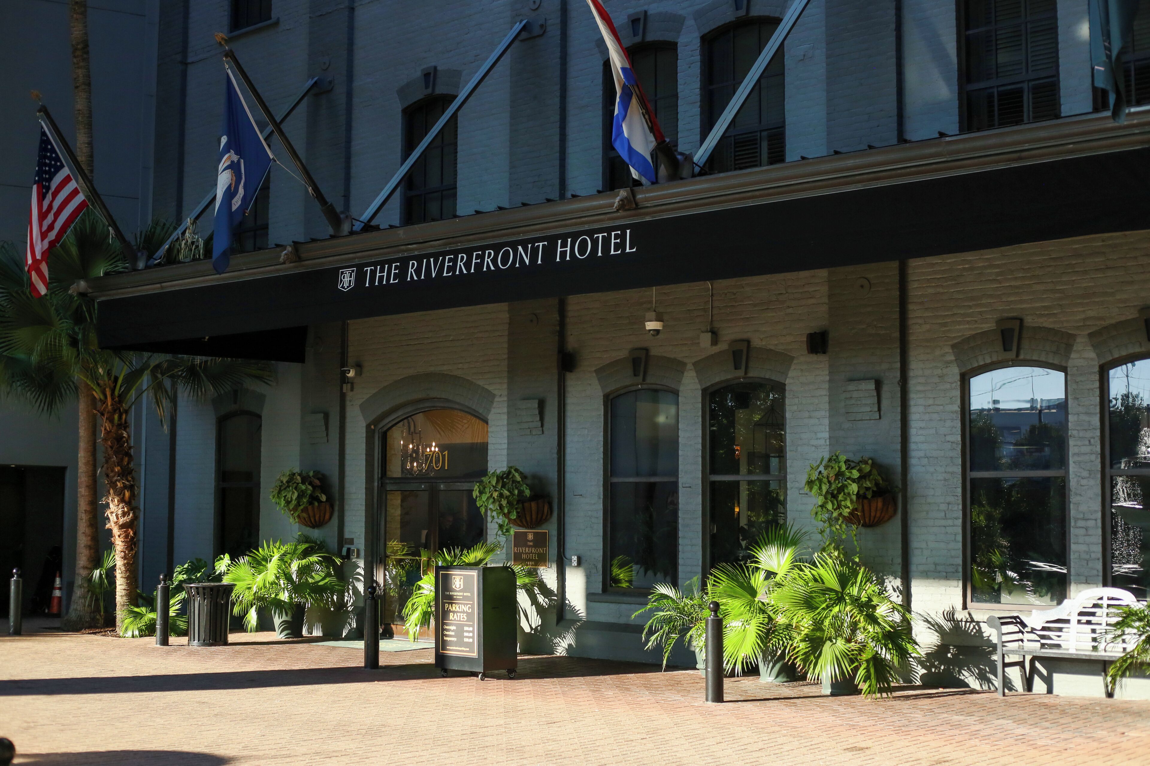 The exterior of The Riverfront Hotel with a brick facade, large windows, and multiple flags.