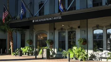 The exterior of The Riverfront Hotel with a brick facade, large windows, and multiple flags.