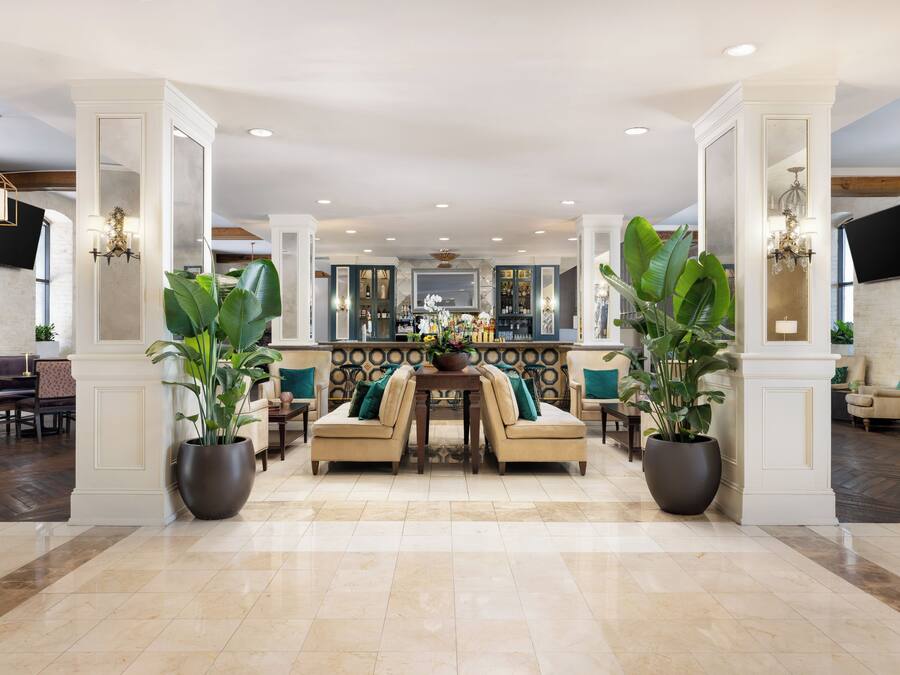 A spacious lobby with a central seating area, large potted plants, and a modern bar setup.