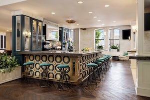 A bar area with a long counter, multiple stools, and a variety of bottles.
