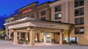 Ein Hampton Inn Hotel mit modernem Design, das einen gut beleuchteten Eingang und eine deutliche Schildtafel mit Namen und Lage zeigt.