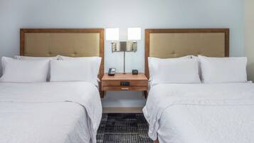 A hotel room with two beds, a bedside table with a lamp, a phone, and a digital clock.