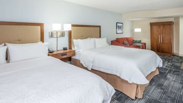 A hotel room with two beds, a desk, a wardrobe, and a red sofa.