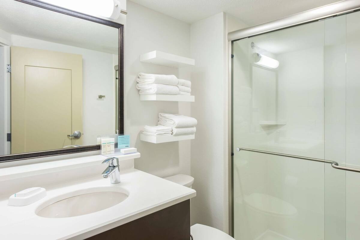 A modern bathroom with a sink, mirror, towel rack, and glass shower enclosure.