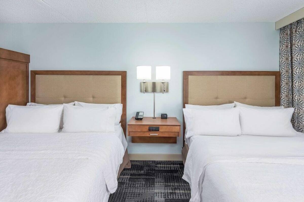 A hotel room with two beds, a nightstand with a lamp, and a patterned curtain.