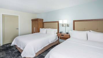 Habitación de hotel con dos camas, un armario de madera, una mesita de noche con lámpara y una puerta.