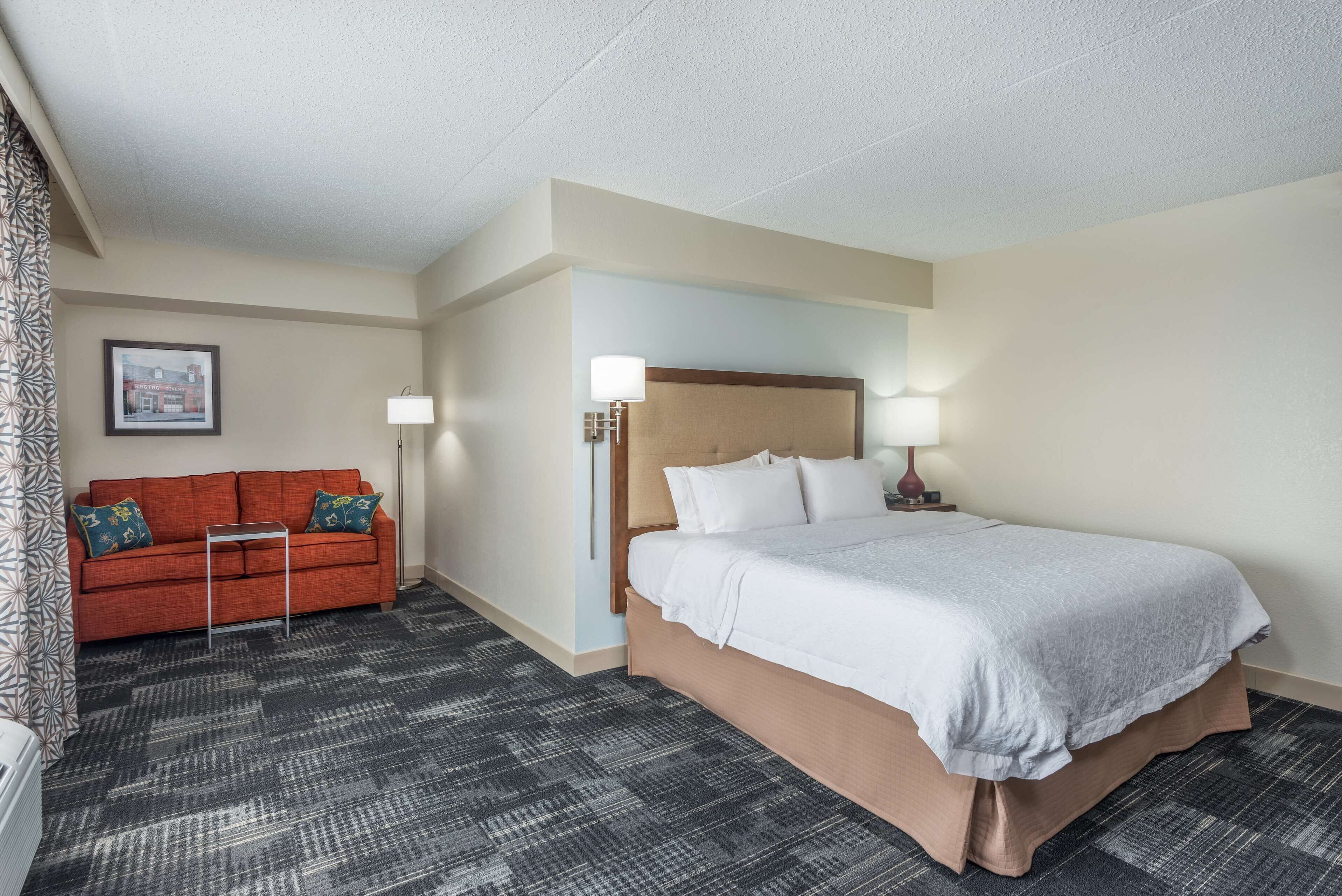 A hotel room with a bed, a sofa, a small table, and a lamp.