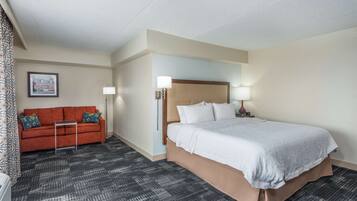 A hotel room with a bed, a sofa, a small table, and a lamp.
