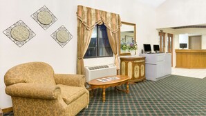 A room with a patterned armchair, a small round table, a desk with a computer, and a mirror.