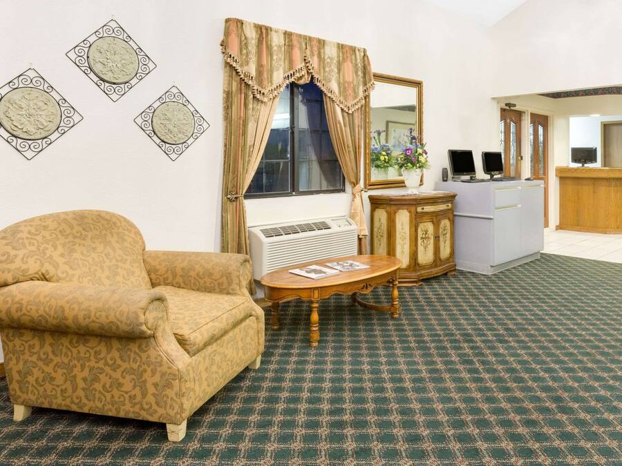 A room with a patterned armchair, a small round table, a desk with a computer, and a mirror.