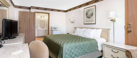 A hotel room with a bed, a desk, a chair, a television, a bedside table, and a nightstand.