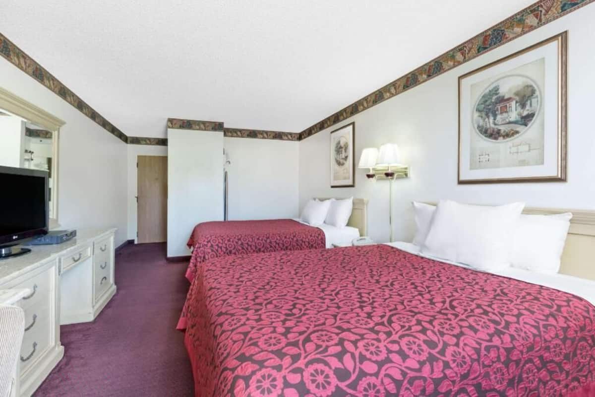 Una habitación de hotel con dos camas, un televisor, un aparador y una puerta que da a un baño.