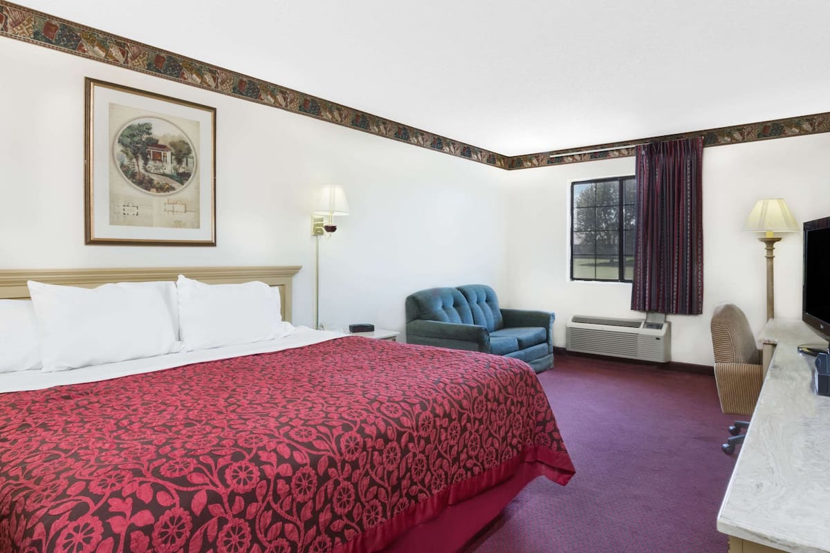 Habitación de hotel con una cama grande, un escritorio, una silla, un televisor y una ventana con cortinas.