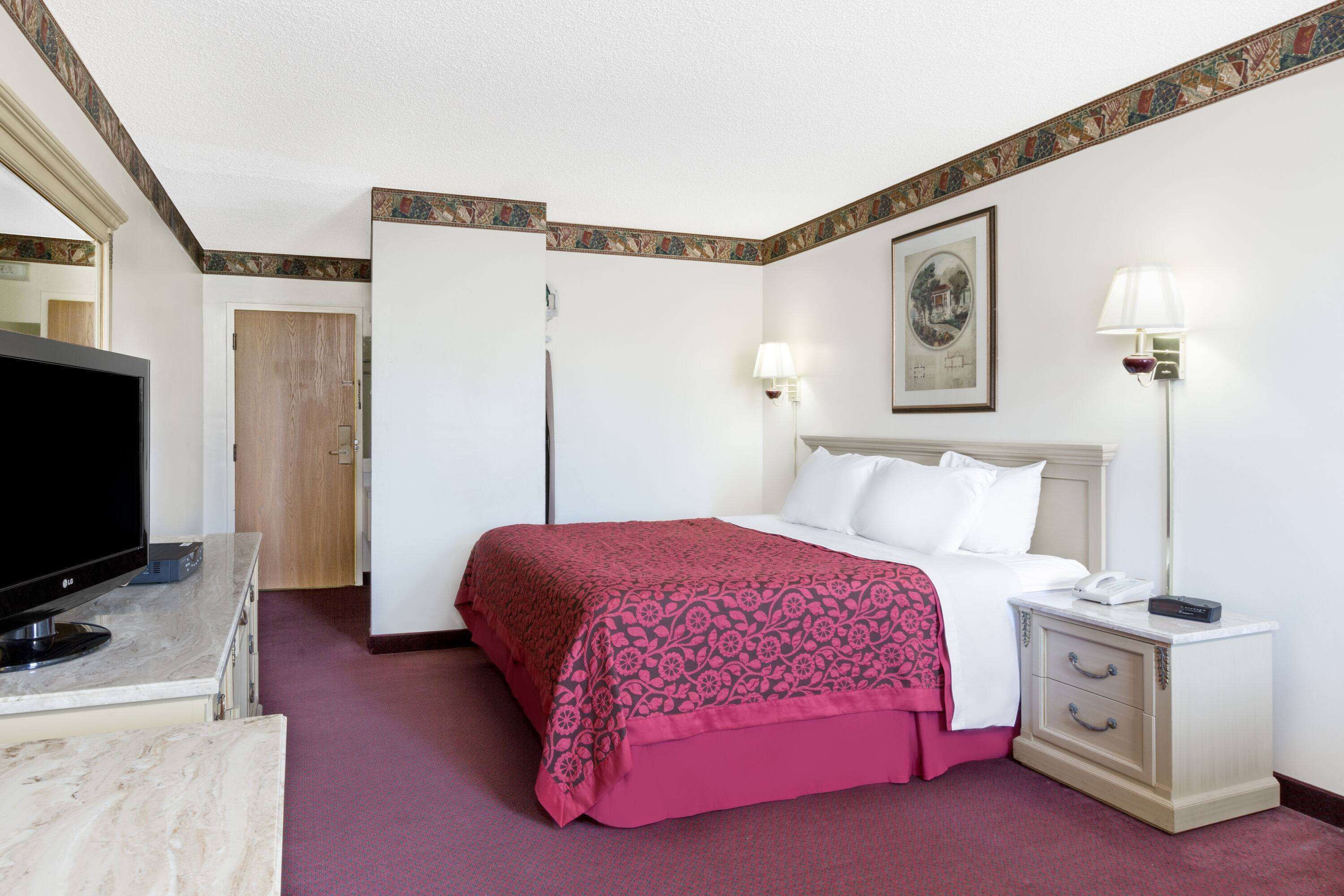 Una camera d'albergo con un letto, lampade sui comodini, una TV e una scrivania con un computer.