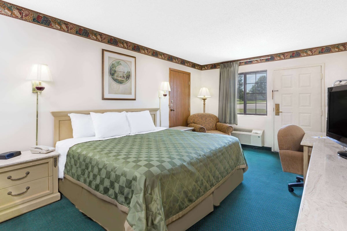 Una habitación de hotel con cama, escritorio, silla, televisor y ventana.