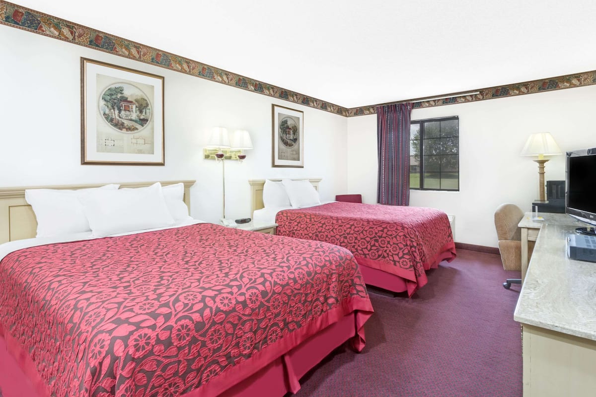 Habitación de hotel con dos camas, un escritorio con televisor y cuadros en las paredes.
