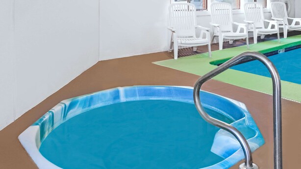 A small indoor swimming pool with a metal ladder, surrounded by white chairs.