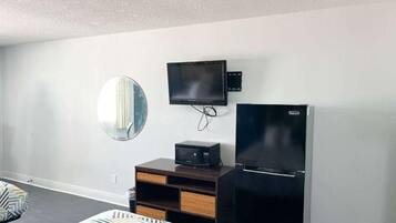 Ein Hotelzimmer mit einem Bett, einem flachbildfernseher an der Wand, einem Kühlschrank, einem kleinen Nachttisch und einem Spiegel.