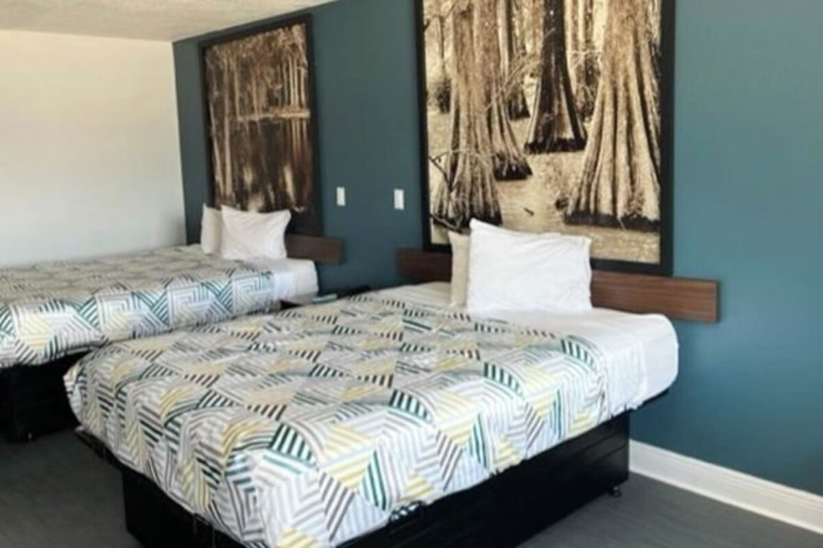 A hotel room with two beds, a large painting on the wall, and a dark blue accent wall.
