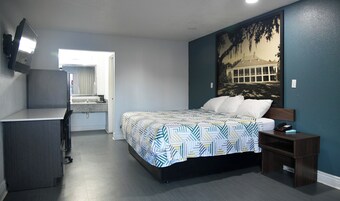 A bedroom with a bed, a desk, a chair, a TV, and a painting on the wall.