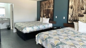 A hotel room with two beds, a nightstand, a bathroom with a sink, and a large abstract painting on the wall. - Studio 6 Suites Opelousas, LA (Opelousas)