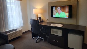 Een hotelkamer met een bureau, stoel, airconditioning, lamp, televisie en een minibar.