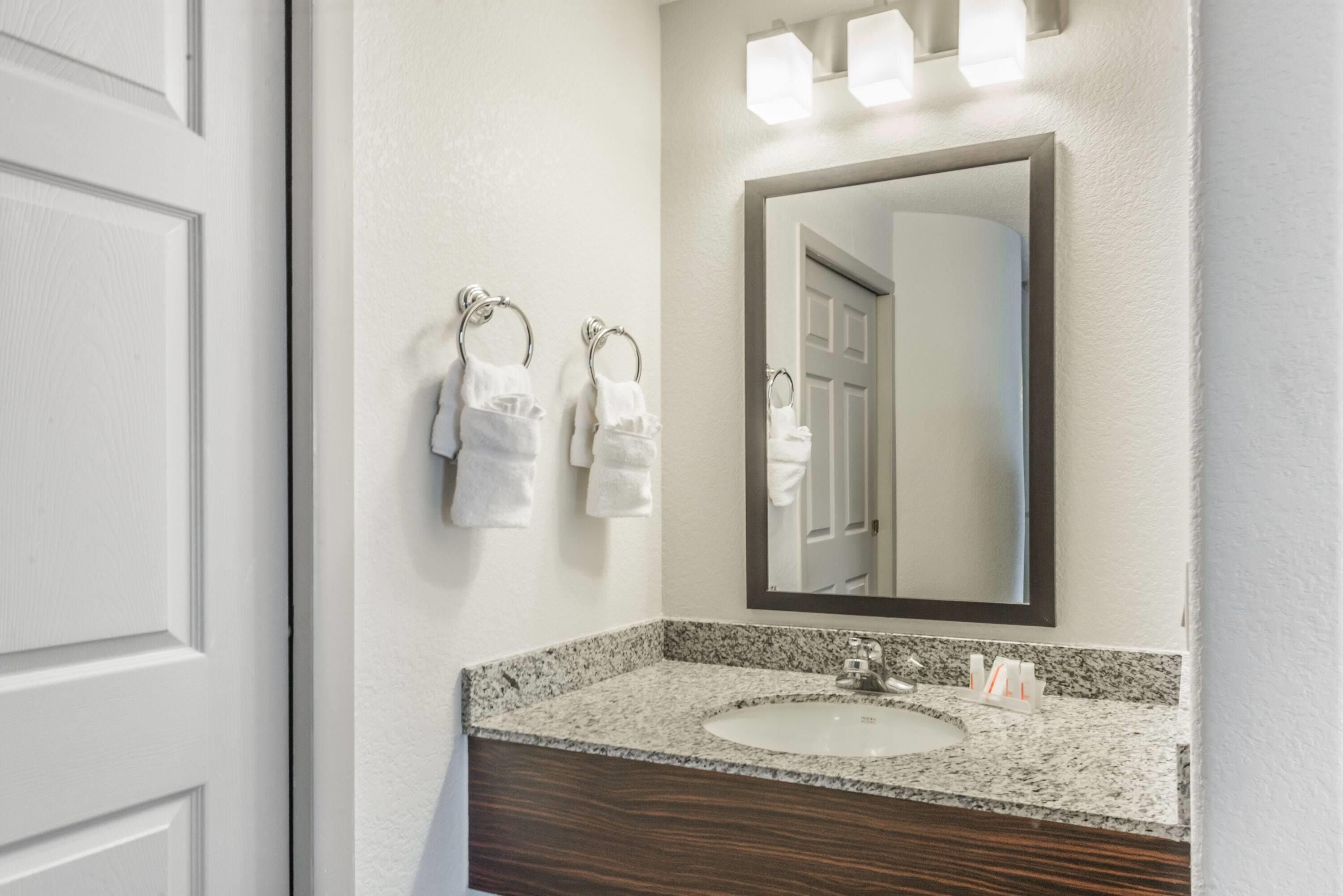 A bathroom with a granite countertop, a sink, a mirror, and two towels hanging on towel rings.