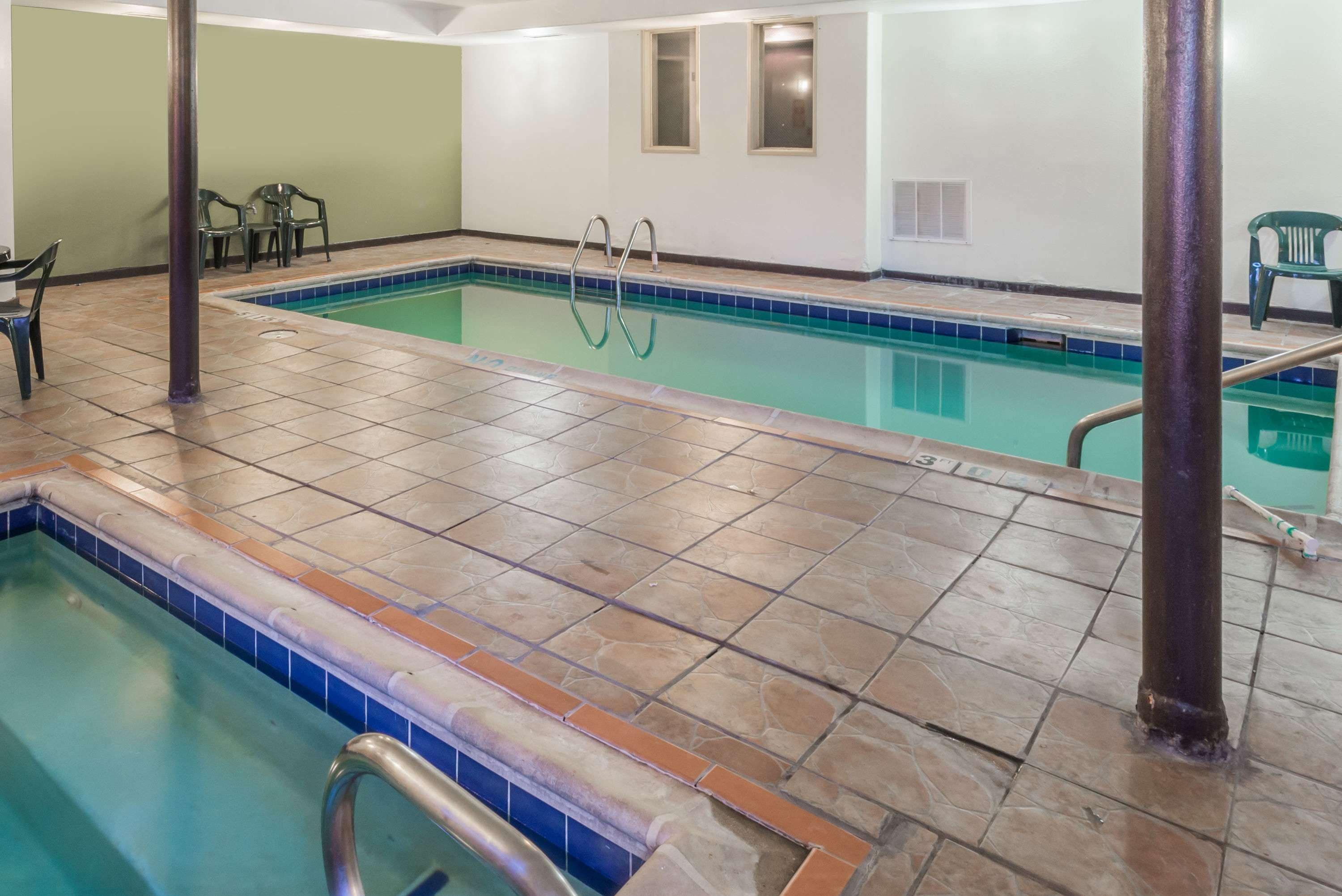 Une piscine intérieure avec un revêtement de sol carrelé, un escalier pour accéder à la piscine et quelques chaises disposées autour de la piscine.