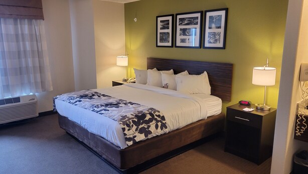 Een hotelkamer met een groot bed, twee nachtkastjes, een wandlamp en een verzameling ingelijste foto's.
