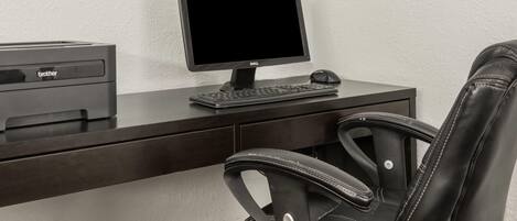 Un bureau avec un écran d’ordinateur, un clavier et une souris, une imprimante et un fauteuil en cuir.
