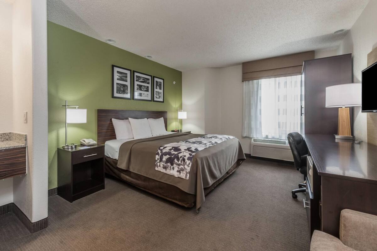 Ein Hotelzimmer mit Bett, Nachttischen, Schreibtisch, Stuhl, Fernseher und gerahmten Bildern an der Wand.