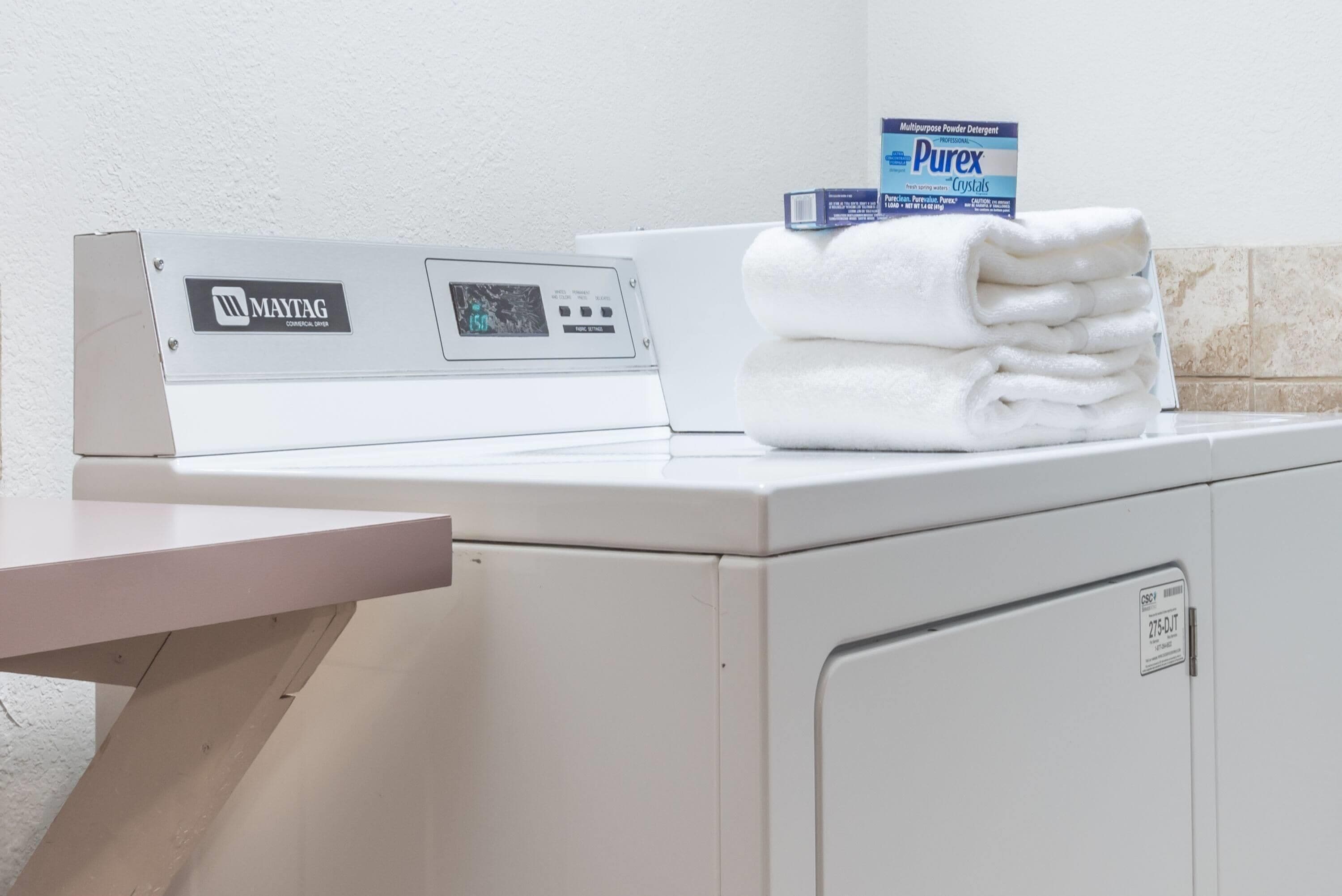Una lavadora Maytag con un panel de control, una pila de toallas blancas y una caja de detergente Purex.